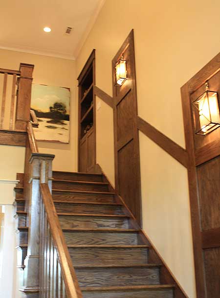 Craftsman style staircase with dark wood wainscoting, built-in shelves, and lantern-style light fixtures.