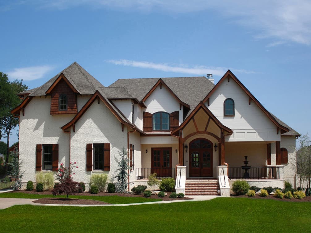 House plan exterior with gabled roofs, dormers, textured siding, and arched entryway with double doors.