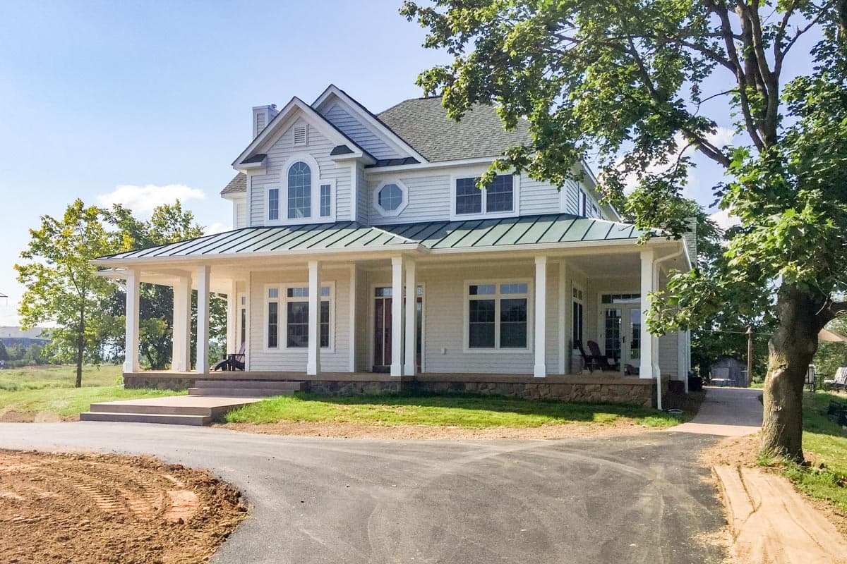 House plan exterior featuring a two-story farmhouse style with a wraparound porch, gables, and a metal roof over the porch.