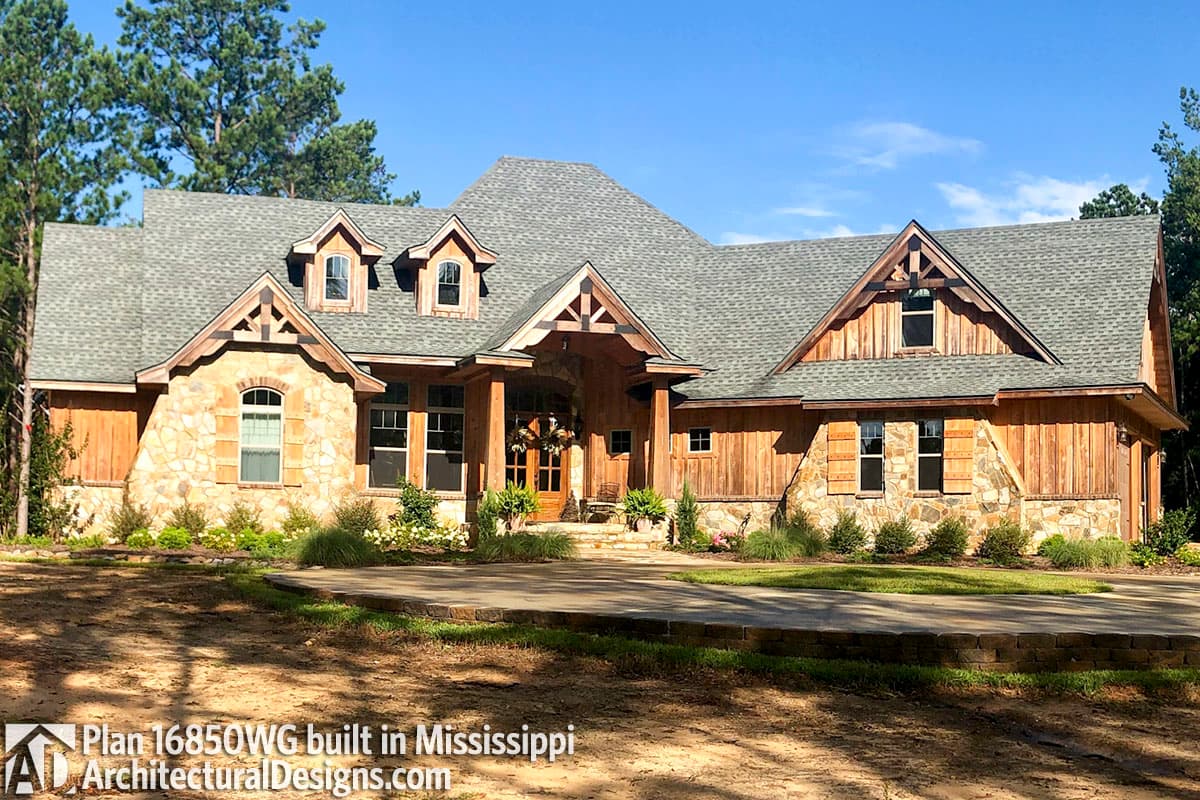 House plan exterior: Lodge style, multiple gables, stone and wood facade, covered entry with timber posts, dormers.