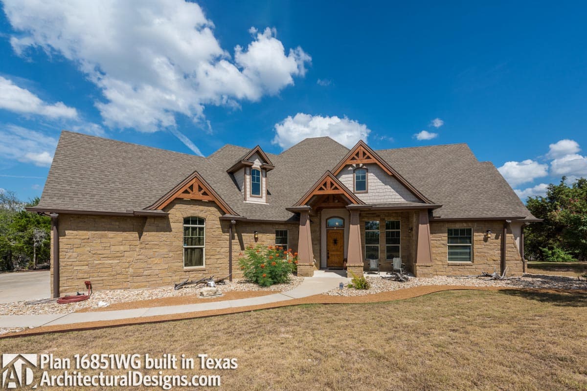 House plan exterior: Two-story home with stone facade, covered entry porch, dormers, and gable accents.