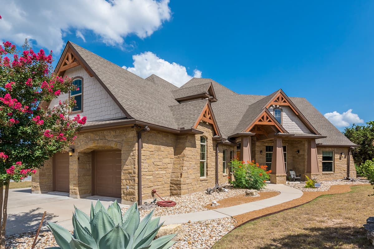 House plan exterior with stone veneer, gabled roof, and wood truss detail over the front porch and gables. Includes a two-car garage.