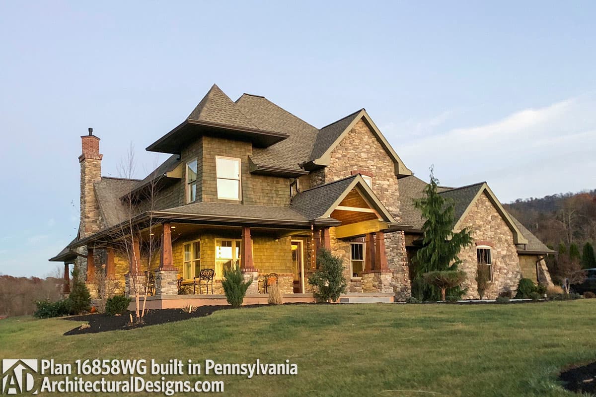 House plan exterior showing a two-story home with a large wrap-around porch, stone accents, and multiple gables.