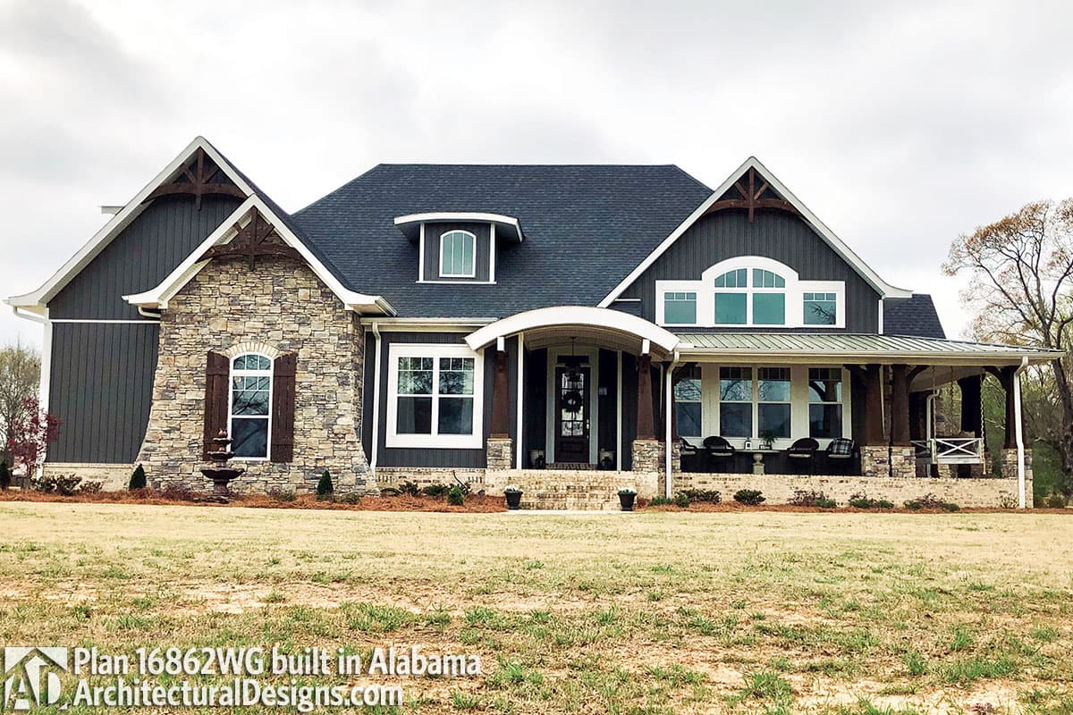 House plan exterior: Modern Farmhouse style, one-story with stone accents, arched dormer, wraparound porch, and decorative gable trusses.
