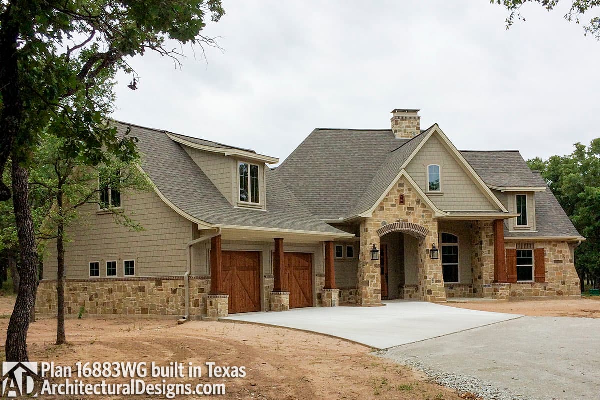 House plan exterior: two-story home with stone accents, arched entry, dormers, gables, and a three-car garage.