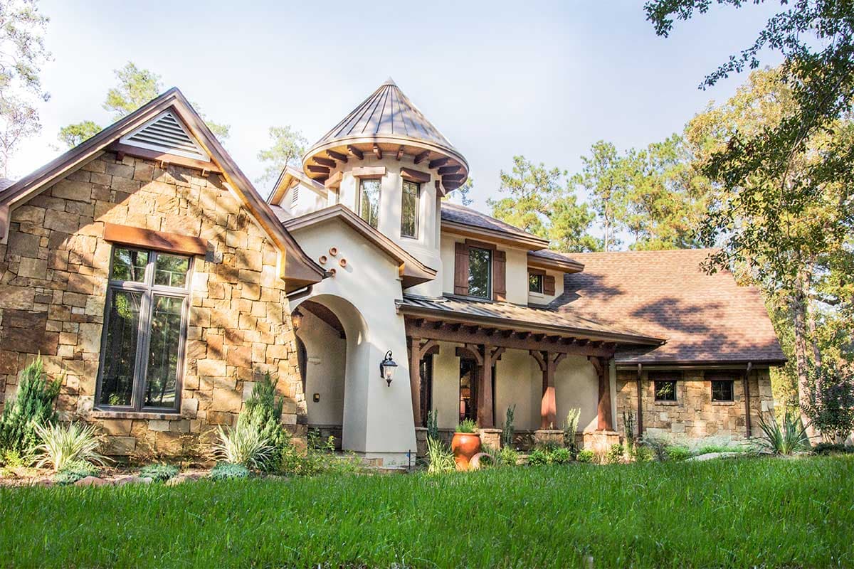 House plan exterior featuring stone facade, arched entryway, conical turret, and covered porch with wooden posts.