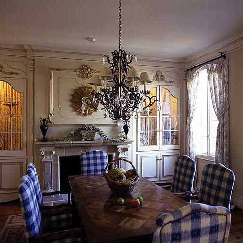 Dining room with ornate fireplace, built-in cabinets, patterned curtains, chandelier, and a wooden table with chairs.