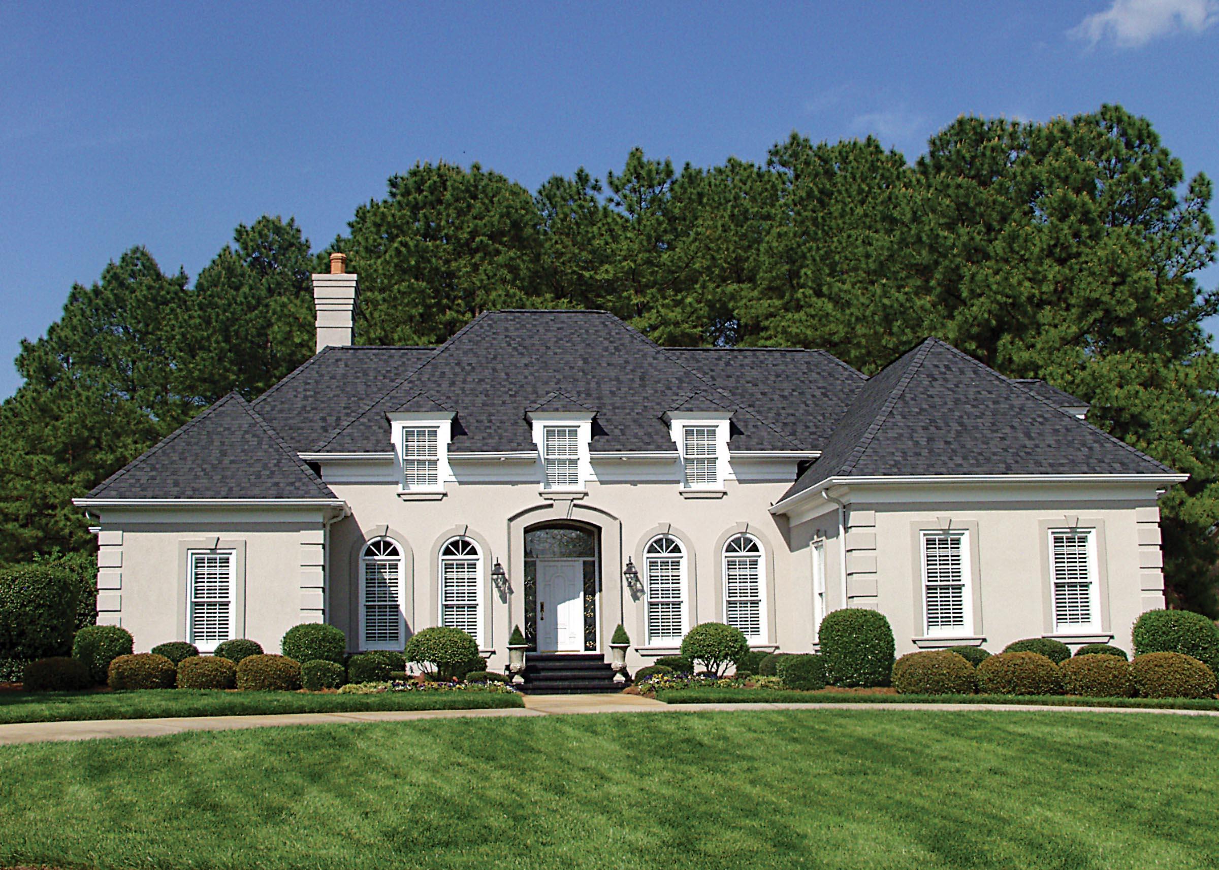 House plan exterior of a large, stucco, one-story home with a central arched entryway, dormer windows, and a prominent chimney.