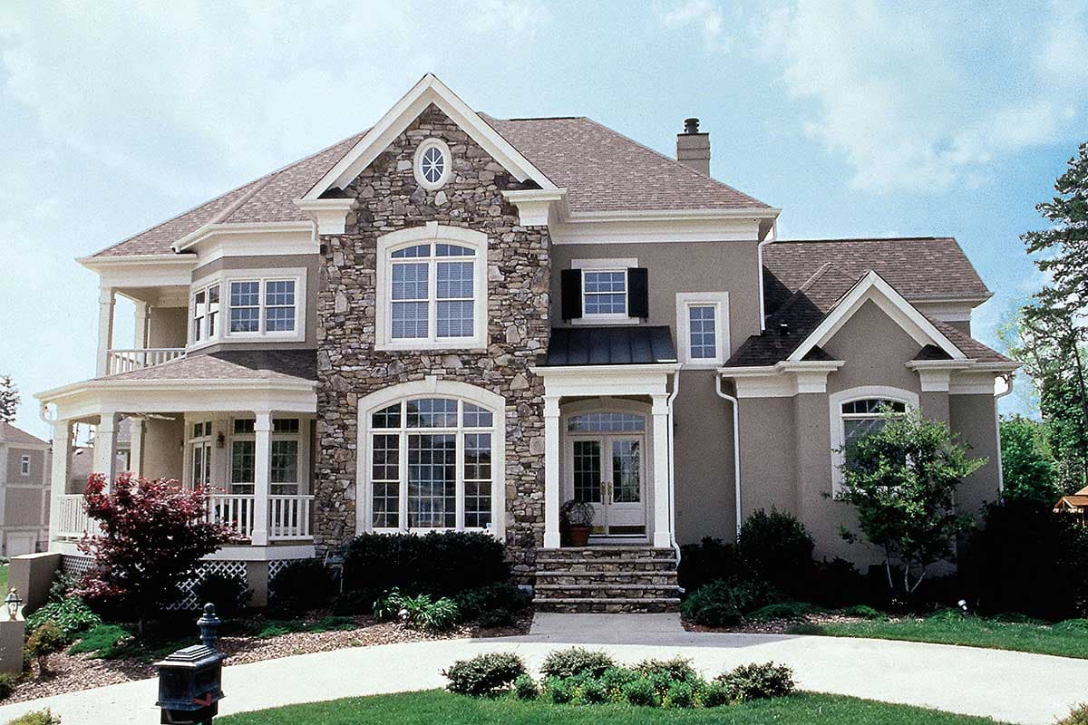 House plan exterior. Two-story with stone facade, multiple gables, arched windows, and a covered porch. Columns support upper-level balcony.