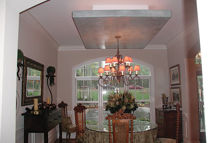 Dining room with a glass-top table, ornate chairs, and a multi-tiered chandelier beneath a coffered ceiling.