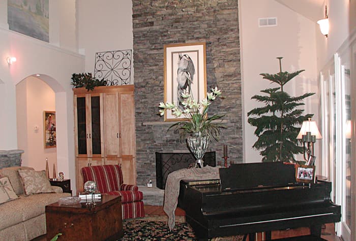 Living room with stone fireplace, vaulted ceiling, grand piano, and tall arched doorway.