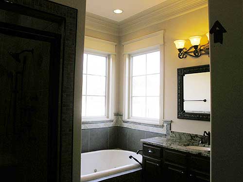 Bathroom with jetted tub, tiled walls, vanity with granite countertop, and a three-light sconce.