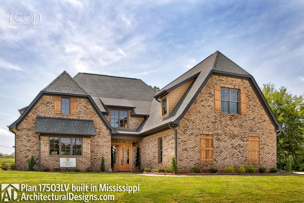 House plan exterior with brick facade, multiple gables, dormers, and wooden shutters.