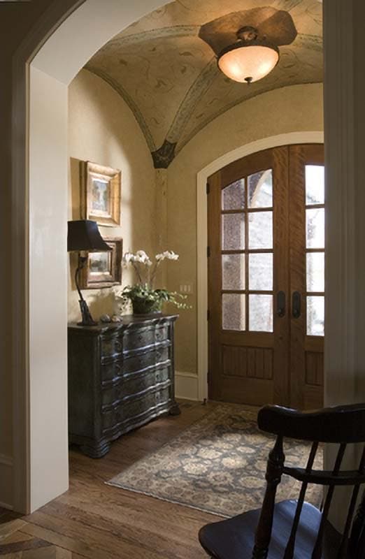 Interior view of a foyer with vaulted ceiling, arched doorway, double paneled wood doors, and a chest of drawers.