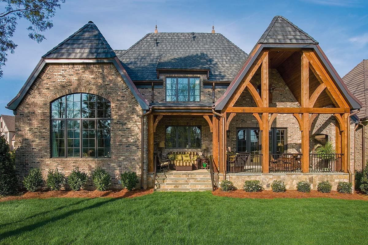 House plan exterior: Brick residence with peaked gables, arched window, timber-framed porch, and steeply pitched roof.
