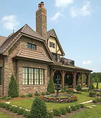 House plan exterior showing brick facade, prominent chimney, arched loggia with timber columns, and tiered rooflines.