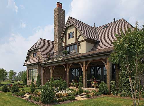 European-inspired house plan exterior with tile roof, stone chimney, covered porch with timber posts, and dormer windows.