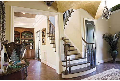 Interior view of a house entry with a curved staircase, built-in bookshelves, and a tray ceiling.