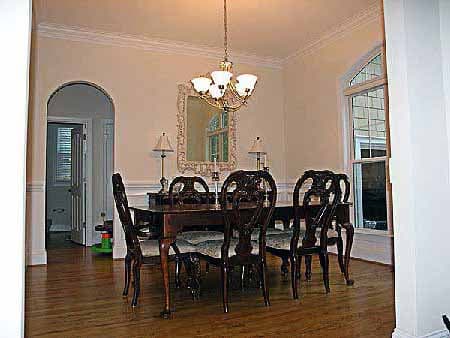 Dining room with dark wood table and chairs, arched doorway to hallway, and large window with arched top.