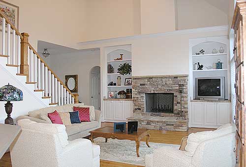 Living room interior with stone fireplace, built-in shelves, a staircase, and upholstered furniture.