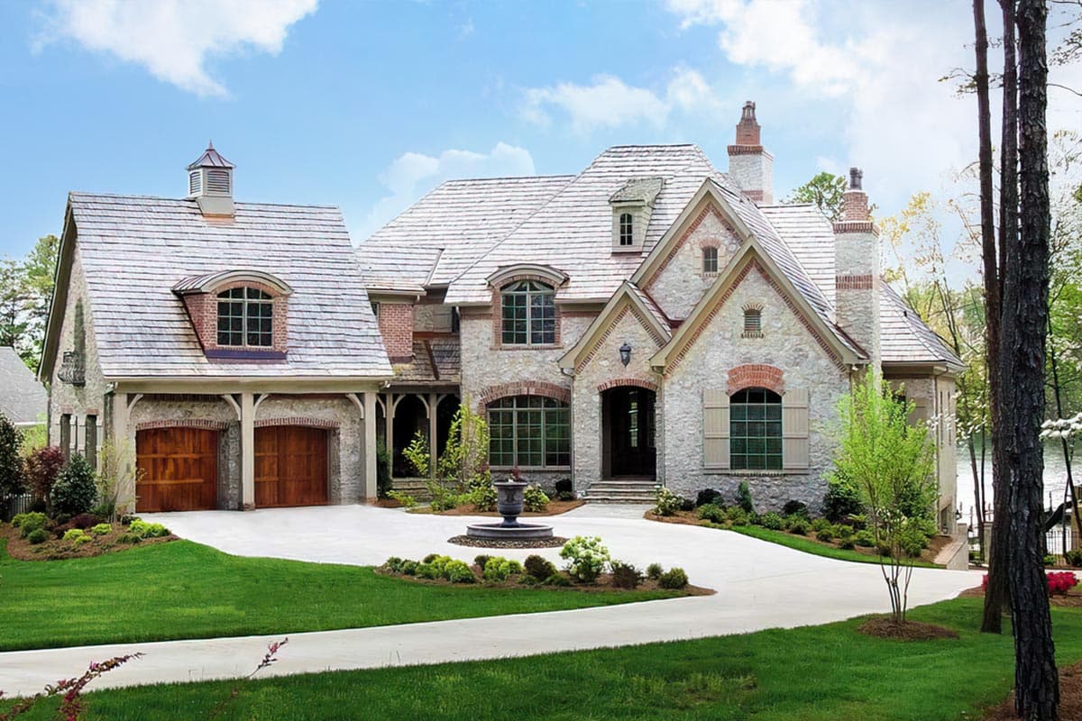 House plan exterior: Stone and brick two-story home with a multi-gabled roof, dormers, and a three-car side-entry garage.