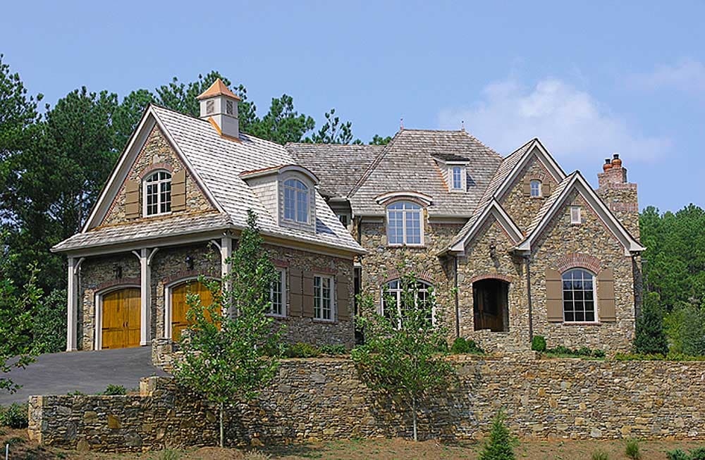 House plan exterior: Stone-clad home with multi-gabled rooflines, arched entry, dormers, and attached three-car garage.