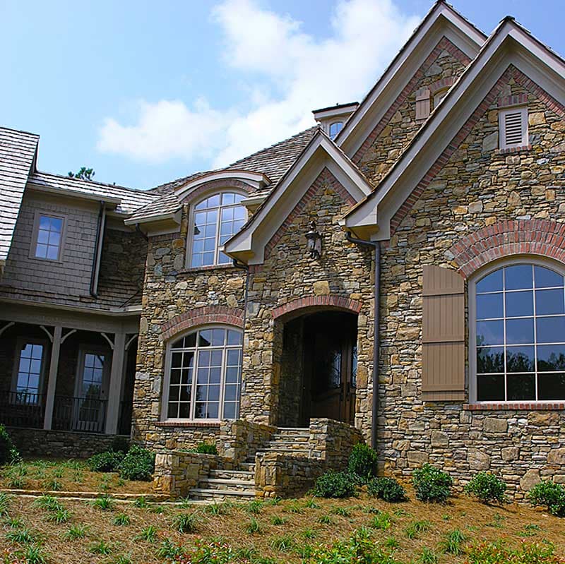 House plan exterior: Stone-clad home with arched windows, prominent gables, and a covered entryway with stone steps.