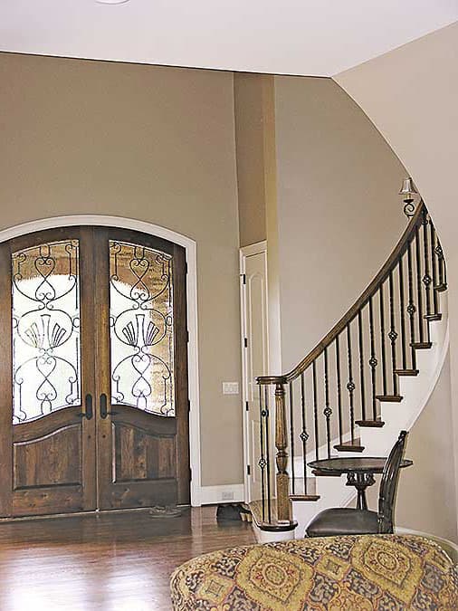 Interior view of a home entry featuring double wooden doors with wrought iron glass panels and a curved staircase with ornate railing.