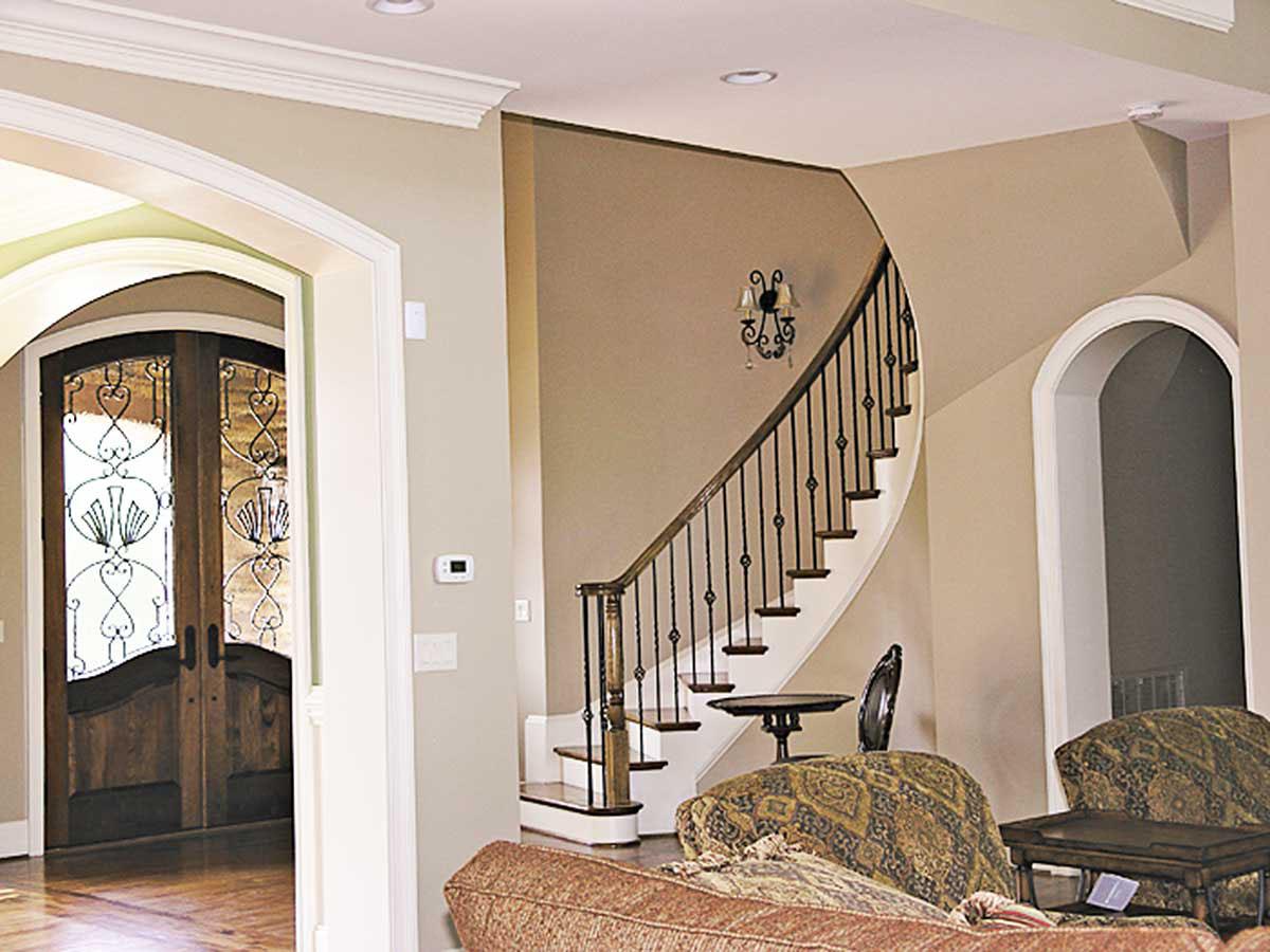 Interior view of a house entrance with a curved staircase, wrought iron railings, and decorative double doors.