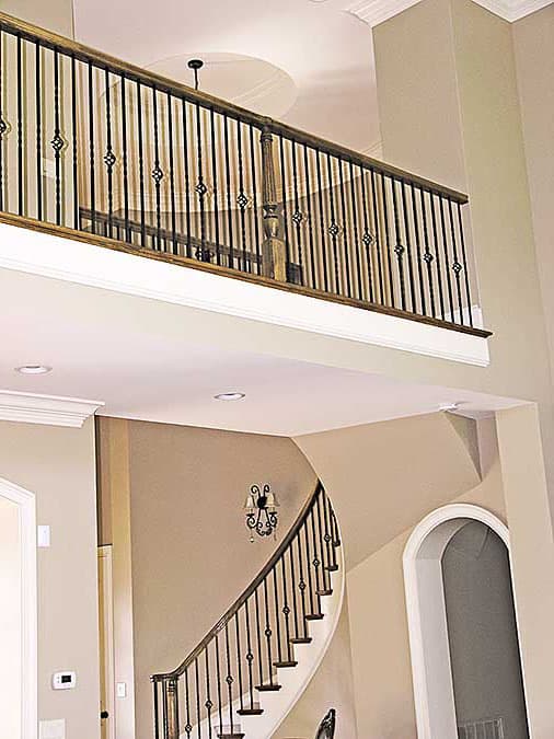 Two-story foyer with curved staircase, ornate metal railings, and upper-level balcony overlooking the entrance.