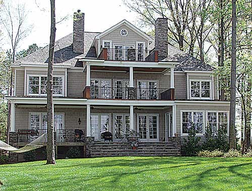 House plan exterior, traditional style, three stories, stone chimneys, multiple balconies, and large windows.