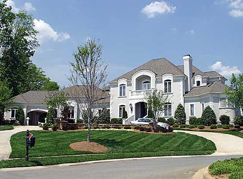 Exterior view of a two-story house plan with arched windows, a balcony, dormers, and a side-entry garage.
