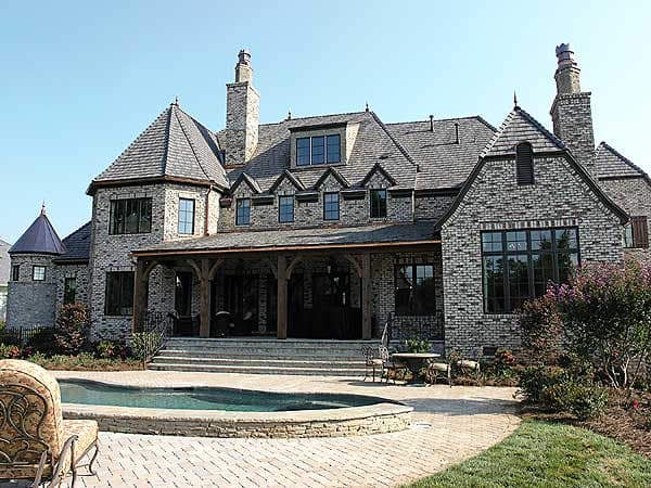 House plan exterior featuring a two-story brick home with multiple gables, dormers, a covered porch, and a turret.