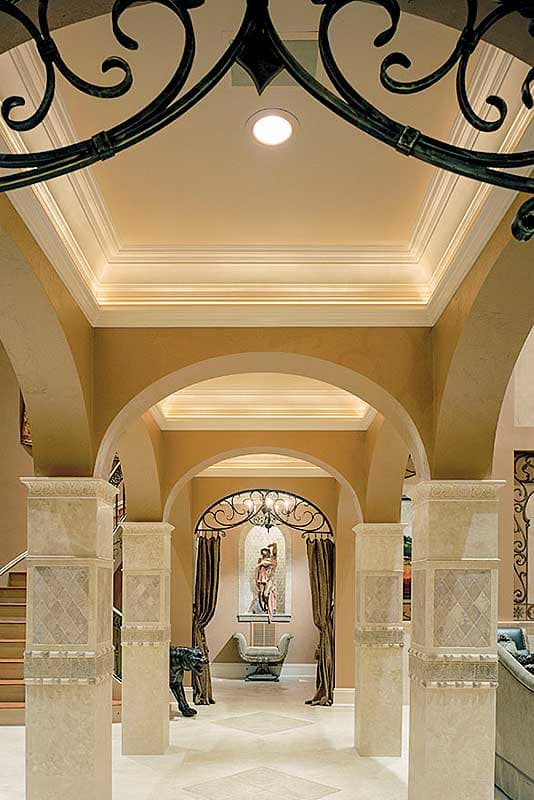 Interior view of a foyer with arched doorways, decorative columns, coffered ceiling, and a sculpture niche.