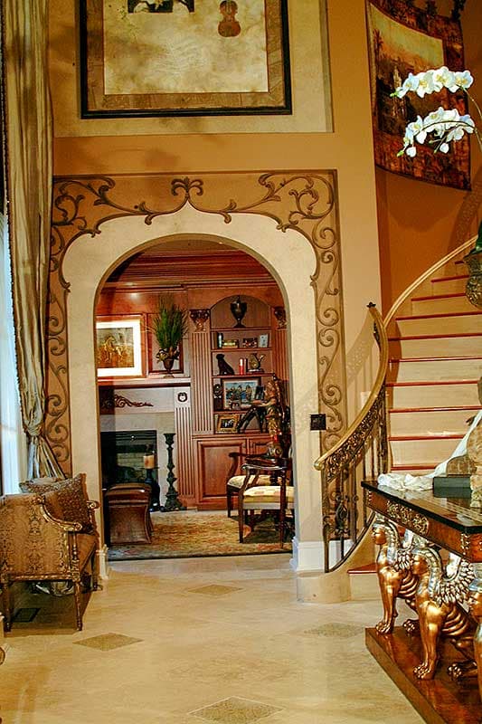 View of living room with fireplace, built-in bookshelves, and curved staircase with ornate railing.