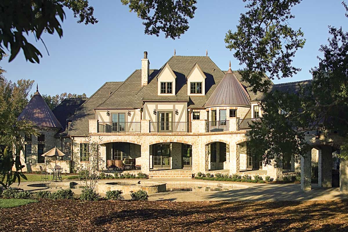 House plan exterior of a multi-story stone home with arched loggias, balconies, multiple gables, and a conical turret.