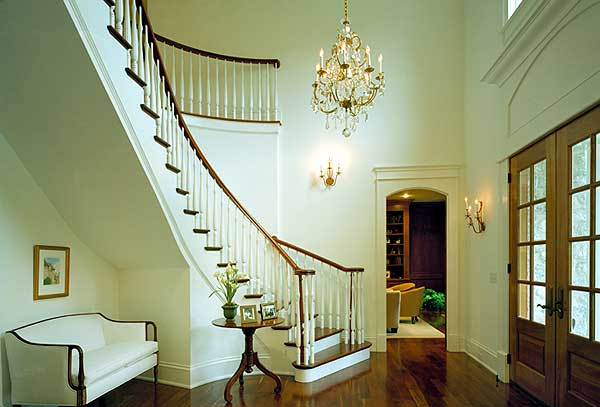 Foyer with a curved staircase, crystal chandelier, and double wood doors.