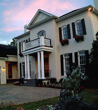 House plan exterior: two-story brick home with prominent portico, balcony, and black shutters.