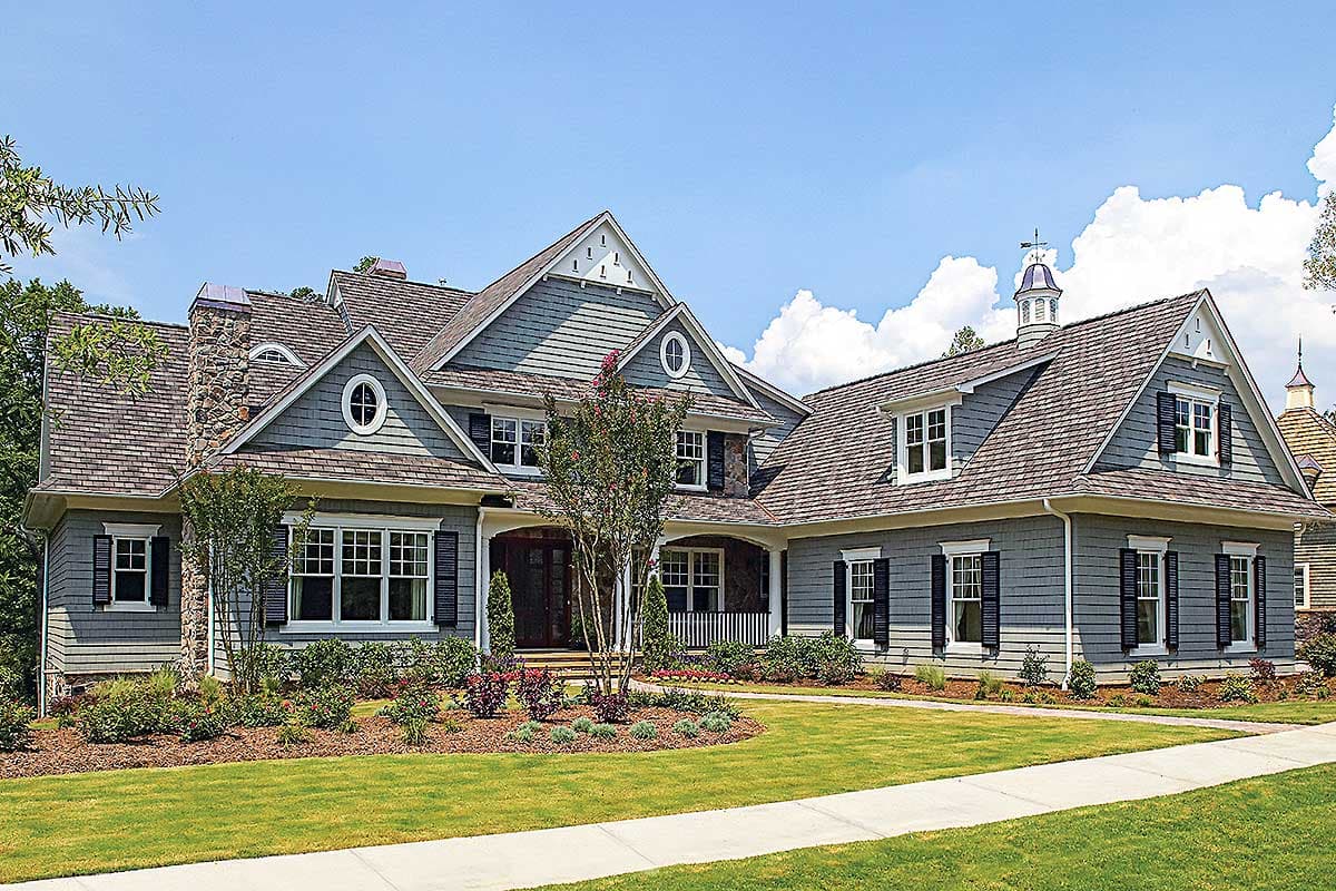 House plan exterior with multiple gables, shake roof, and a covered porch. Features include oval and rectangular windows and multiple dormers.