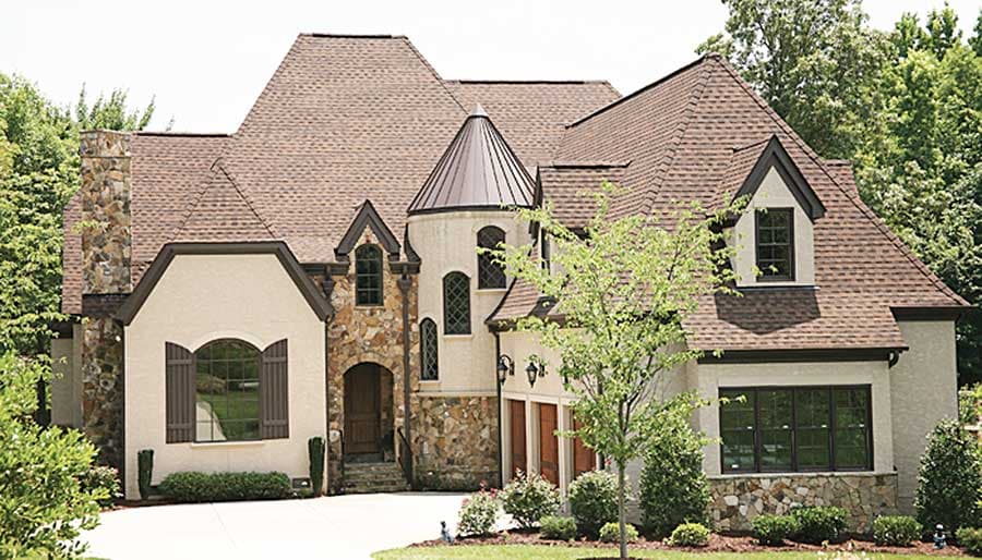 House plan exterior showing a multi-story residence with a stone facade, prominent gables, and a conical tower.