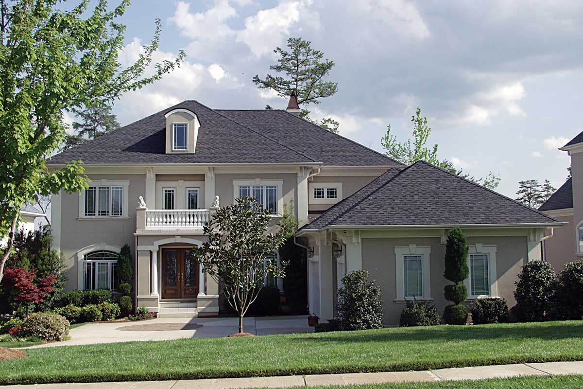 House plan exterior with two stories. Features include a front porch with balustrade, multiple gables, and a dormer. The garage is attached.