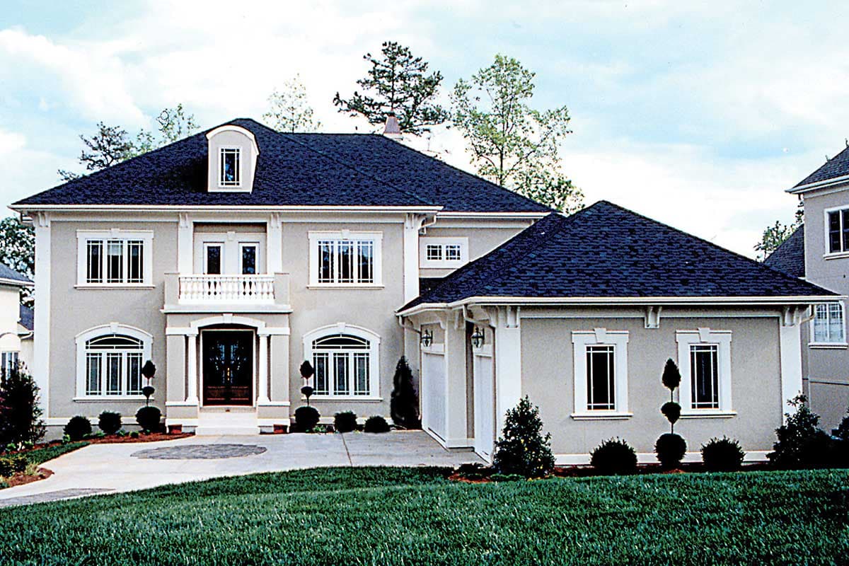 House plan exterior: Two-story stucco home with a centered arched entry, second-story balcony, dormer, and attached garage.