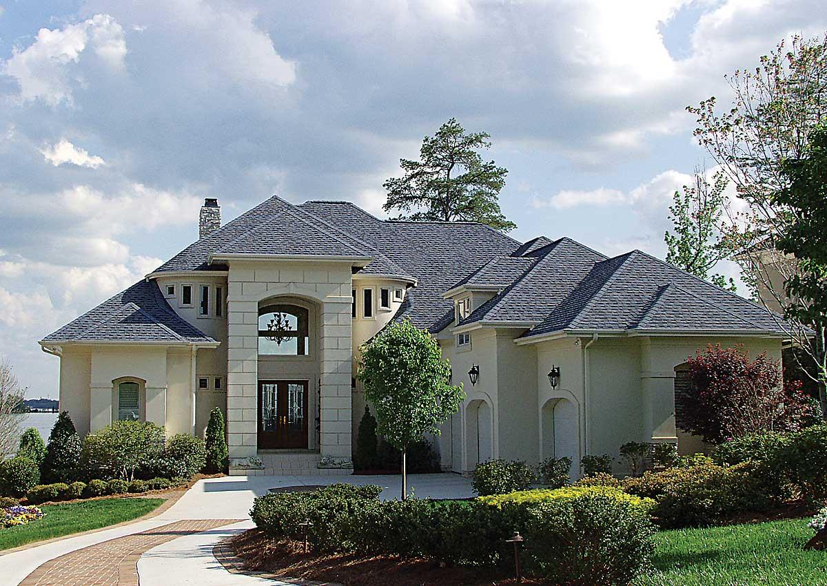 House plan exterior: two-story estate with grand arched entry, stone accents, multiple gables, and attached garages.