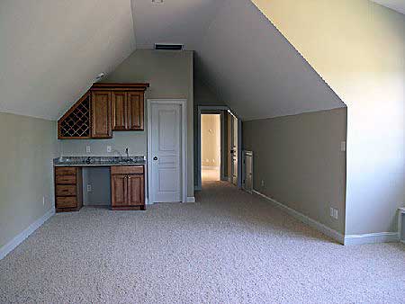 Interior view of a room with sloped ceilings, featuring a wet bar with wine rack and cabinets, and a doorway leading to another room.