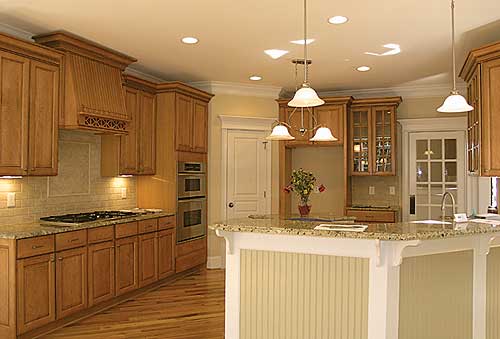 Kitchen interior with wood cabinetry, granite countertops, island with pendant lights, and stainless steel appliances.