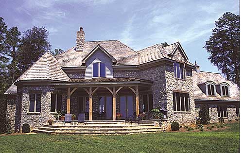 House plan exterior showcasing a two-story stone home with a covered porch, dormers, and a turret with a conical roof.