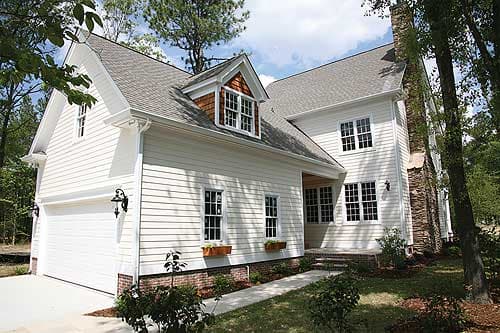 House plan exterior: two-story white home with gabled dormer, stone chimney, and attached garage.