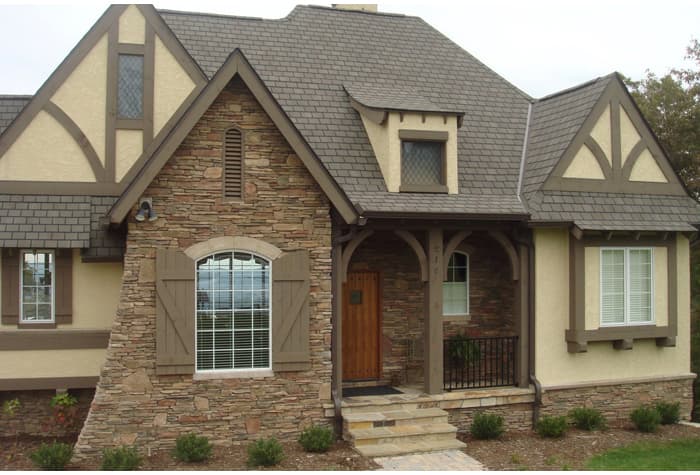 House plan exterior with stone facade, arched window, timber framing, covered porch with arched supports, and dormer.