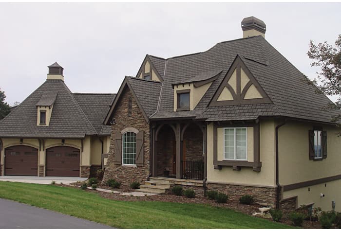 European-inspired house plan exterior with a side-entry garage, stone accents, prominent gables, and arched porch supports.