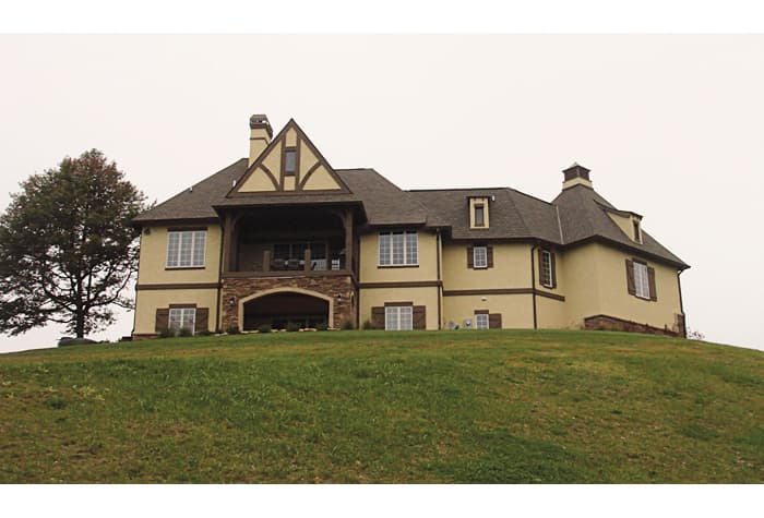 House plan exterior: two-story Tudor style with covered porch, stone archway, dormers, and prominent gable.